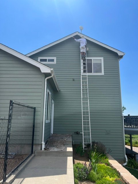 Painter on a ladder painting the trim of a sage green gable