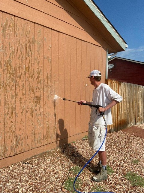 Crew member power washing siding before painting